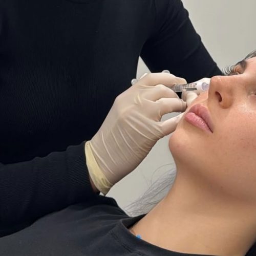 A woman lies back as a gloved professional injects a syringe into the area beneath her eye, performing a cosmetic procedure.